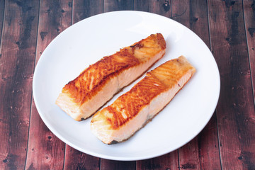 2 Grilled salmon steaks on white plate served on wood.