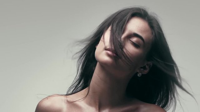 Young woman with wind in hair shot in slow motion on gray