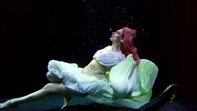 Incredible woman dressed like underwater princess posing in darkness. Exotic woman floating in a dark pool.