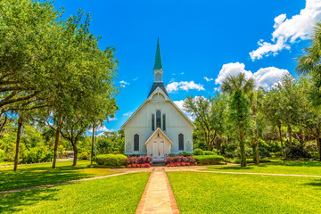 A small white Methodist church down a brick walk under blue skies - Powered by Adobe