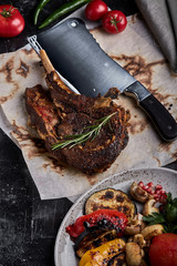 Tomahawk steak with vegetables and a knife on the table. Grilled meat with grilled vegetables and...