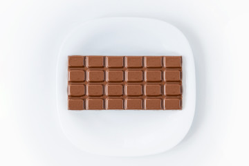 Chocolate on white plate on the white table. Dieting, unhealthy lifestyle concept