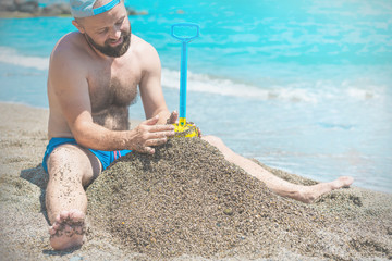 Funny mature man plaing in the sand on tropical beach, Building sand castle