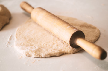 Classic wooden rolling pin with freshly prepared dough and dusting of flour on white background