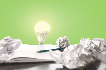 Ideas / trial and error concept image with scrunched paper, pencil and light bulb lighting up.