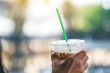 A woman holding a plastic glass of iced coffee with straw
