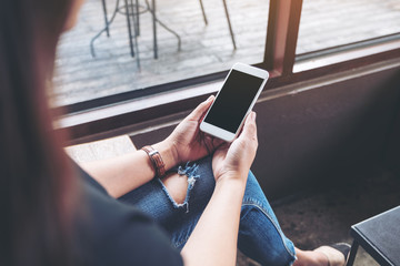 Mockup image of a woman holding white mobile phone with blank black desktop screen in cafe