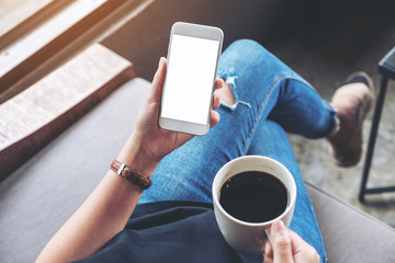 Mockup image of woman holding white mobile phone with blank screen while drinking coffee in cafe