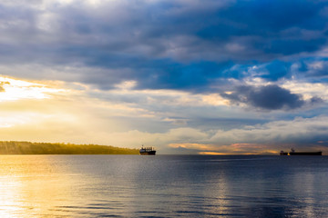Obraz premium Cargo ships at cloudy sunset in bay near Vancouver, BC, Canada.