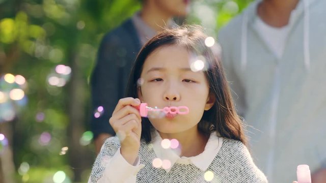 beautiful little asian girl blowing bubbles in park