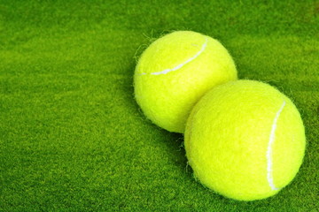 Two yellow tennis ball on the green grass lawn of court in corner