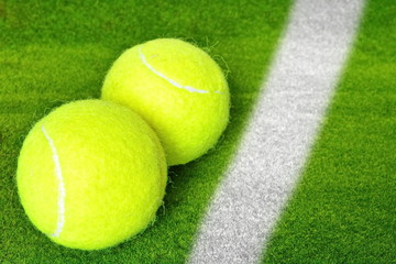 Two yellow tennis ball on the green grass lawn of court behind the white line