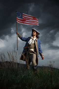 American revolution war soldier with flag of colonies over dramatic landscape. 4 july independence day of USA concept photo composition: soldier and flag.