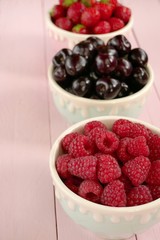 Raspberries, strawberries, sweet cherry berries in  cups set. Summer berries mix on pink pastel wooden background. Berry season.