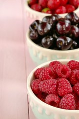 Raspberries, strawberries, sweet cherry berries in round cups . Summer berries mix on pink pastel wooden background. Berry season.