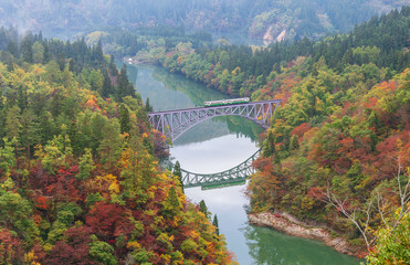 Fototapeta premium First bridge and Tadami river in beautiful autumn season with train crossing the bridge.