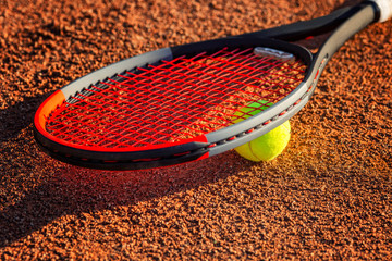 Tennis racket with a ball near the net on the earthen court. Sunny day. Close-up.