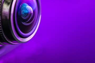 Camera lens and dark purple backlight. Side view of the lens of camera on purple background. Camera Lens Close Up. Optics