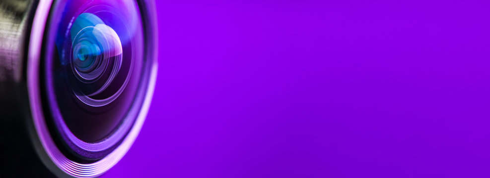 Banner. Camera lens and dark purple backlight. Side view of the lens of camera on purple background. Camera Lens Close Up. Optics