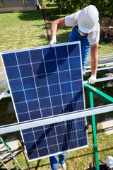 Two mounters installing solar panels on green metallic carcass. Wearing blue uniform, protective helmets. Using special equipment, providing new technologies ecology saving, green energy solution.