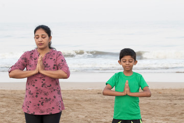 Mother and son doing yoga at beach