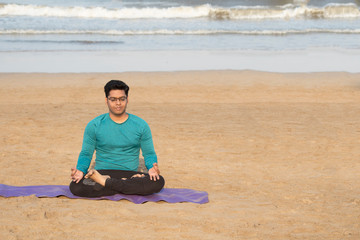 Young man meditating in yoga lotus position at serene beach in morning sunlight