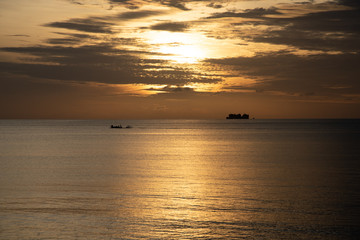 yellow sky of sunset or sunrise in middle frame of the empty space ocean with far little fishing boat in left and little mountain in right stock photo