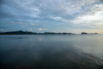 sunset or sunrise on right side of frame reflection seascape beach and mountain in center horizon with cloudy low light weather stock photo