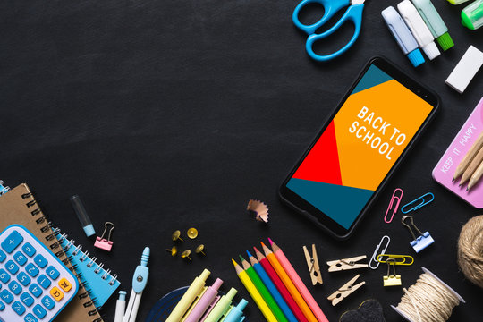 Mock up mobile phone for back to school background concept. School items on black chalkboard background with copy space, top view flat lay background.