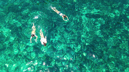 Aerial top view of family snorkeling from above, mother and kids snorkelers swimming in a clear tropical sea water with corals during summer vacation in Thailand