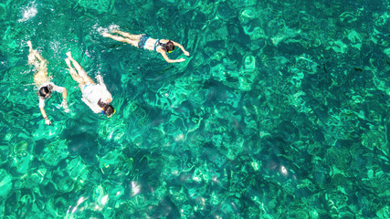 Aerial top view of family snorkeling from above, mother and kids snorkelers swimming in a clear tropical sea water with corals during summer vacation in Thailand