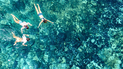 Aerial top view of family snorkeling from above, mother and kids snorkelers swimming in a clear tropical sea water with corals during summer vacation in Thailand