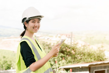 Asian female engineer Put on a white safety hat Wearing a green safety shirt Stand for construction inspection In the construction area