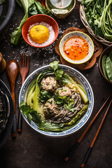 Asian noodles bowl with green vegetables, bok choy and meat balls on dark background with wooden cutlery, chopsticks and hot sauce, top view. Close up. Healthy asian meal. Asian cuisine concept