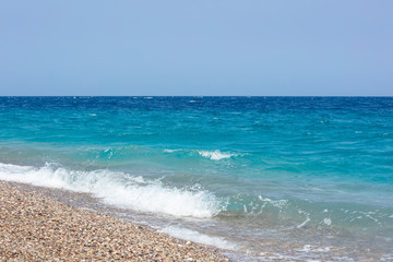 Fototapeta na wymiar Turquoise sea and blue sky in Rhodes, Greece. Waves come to the beach.
