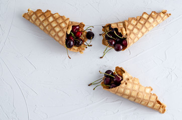 Ice cream cone filled with cherries on a light white concrete background.