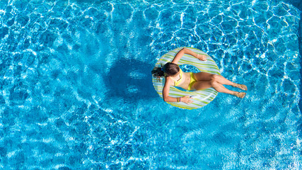 Acrive girl in swimming pool aerial top view from above, kid swims on inflatable ring donut , child has fun in blue water on family vacation resort