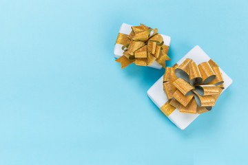 beautiful gift box wrapped in paper with a gold ribbon and a bow on a blue surface. Top view