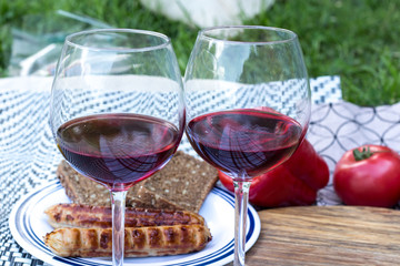 Two glasses of elite red wine. In the background are sausages grilled, vegetables, bread.