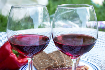 Two glasses of elite red wine. In the background are sausages grilled, vegetables, bread.