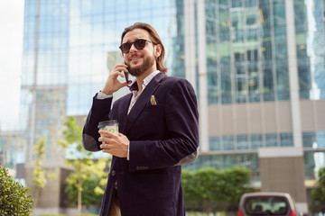 Photo of happy brunet man in sunglasses talking on phone while walking in city