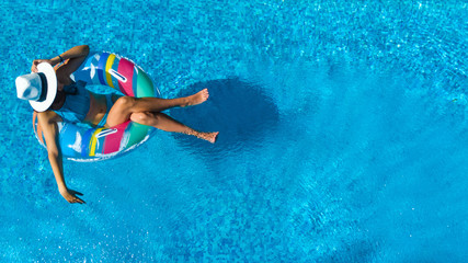 Beautiful girl in hat in swimming pool aerial top view from above, young woman relaxes and swims on inflatable ring donut and has fun in water on family vacation, tropical holiday resort