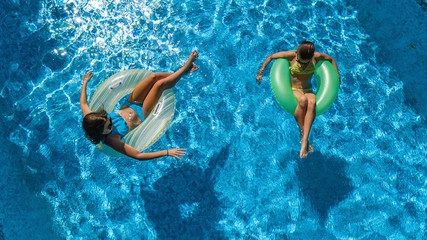 Active children in swimming pool aerial top view from above, happy kids swim on inflatable ring donuts and have fun in water on family holiday vacation on resort