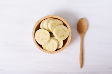 Fototapeta na wymiar Sliced banana in a bowl and wooden spoon on white background, top view