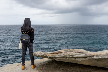 Young woman standing on a cliff watching the rough sea on a bad weather day