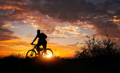Silhouette of sports person cycling on the meadow on the beautiful sunset. Young man with camera...