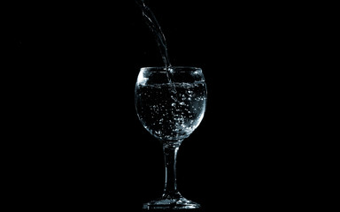 Pour water into glass on black background.