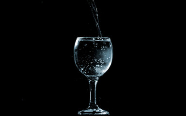 Pour water into glass on black background.