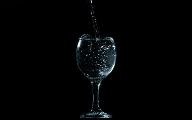 Pour water into glass on black background.