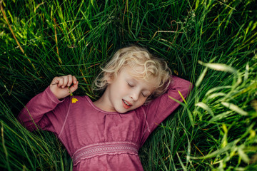 Smiling sleeping dreaming Caucasian girl with closed eyes lying in grass holding yellow bulbous...